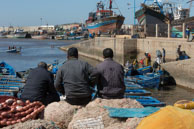 Watching the catch being landed / Three men sitting on fishing nets watching the blue fisking boats at Essaouira (Morocco) landing the catch
