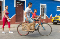 Exercising a caged bird / A Cuban man taking his boy and caged bird for a bike ride in Trinidad