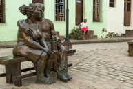 Couple and Old Woman / Statues of a couple on a bench with an old Cuban woman sitting on her door step behind in Camaguey