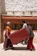 Business goes on / Monks carrying on business (moving stuff) whilst a worshipper spins the prayer wheels